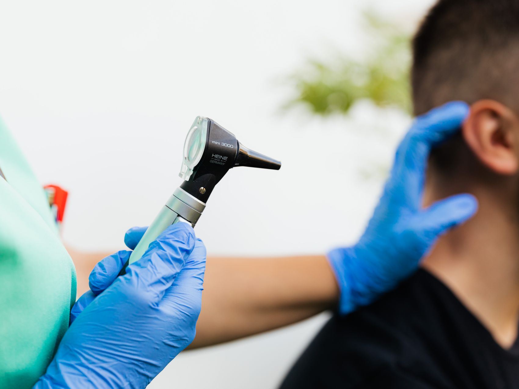 A clinician holds an otoscope near a patient's ear during an examination.